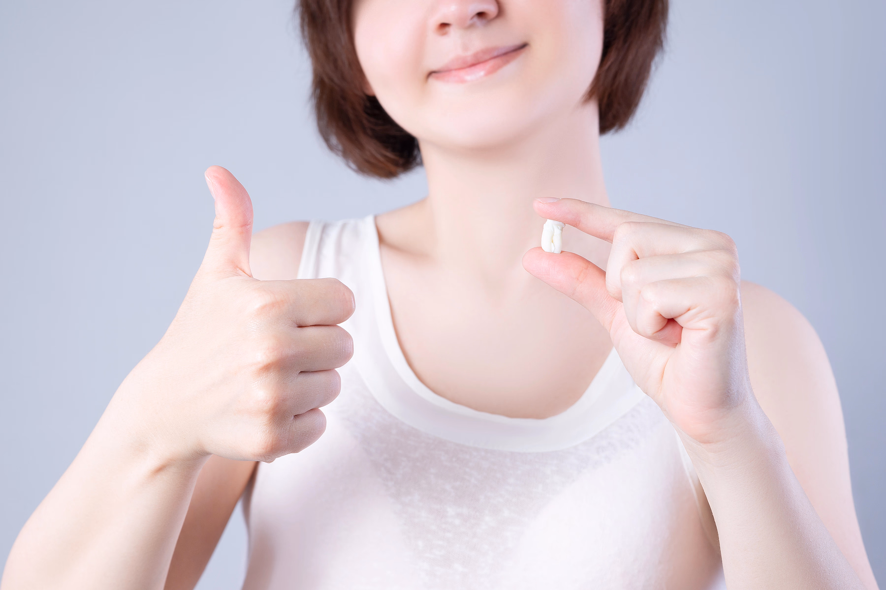 Persona sonriendo y sosteniendo un diente extraído entre el pulgar y el índice, mientras con la otra mano hace un gesto de aprobación con el pulgar hacia arriba.
