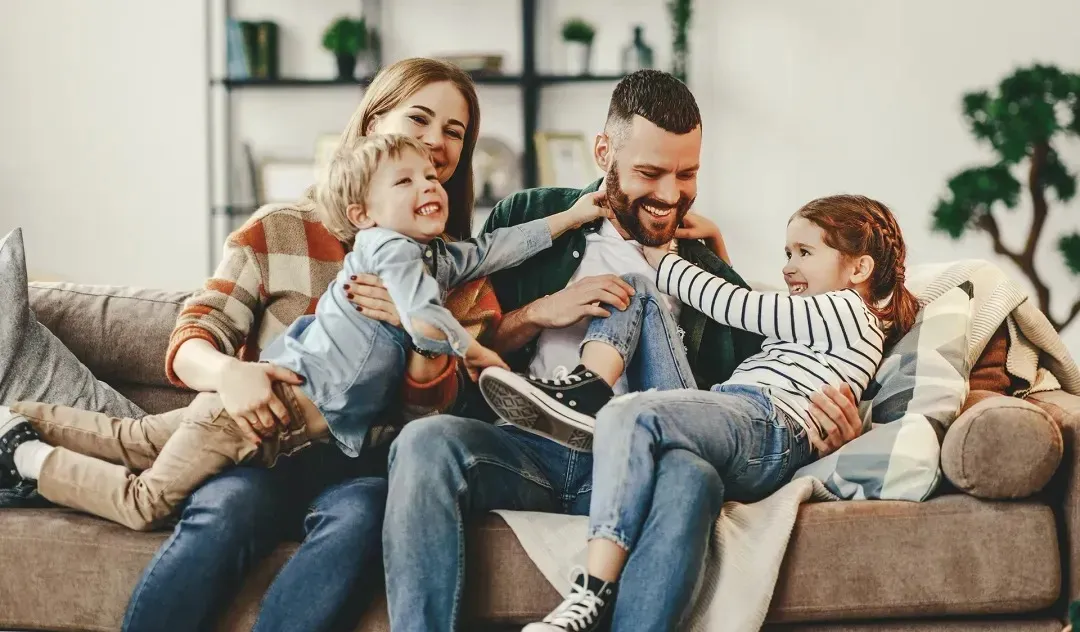 Padres sonrientes jugando y divirtiéndose con sus dos hijos en el sofá de la sala.