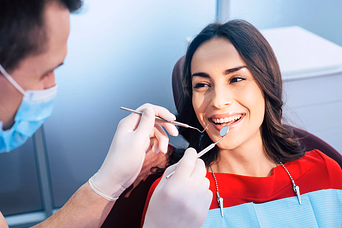 Dentist examining a smiling woman’s teeth during a dental checkup.