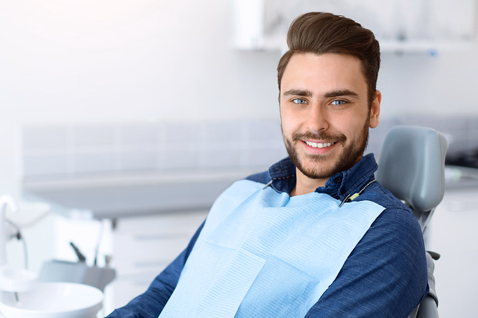 Hombre sonriente sentado en una silla dental con un babero dental azul.
