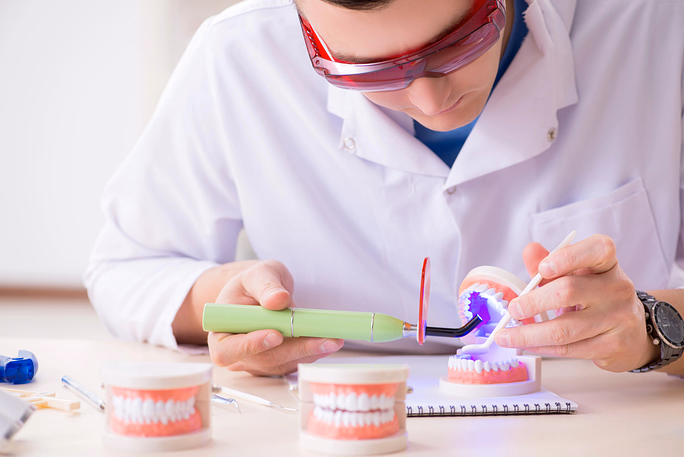 Dentist using a dental curing light on a set of artificial teeth in a dental model.