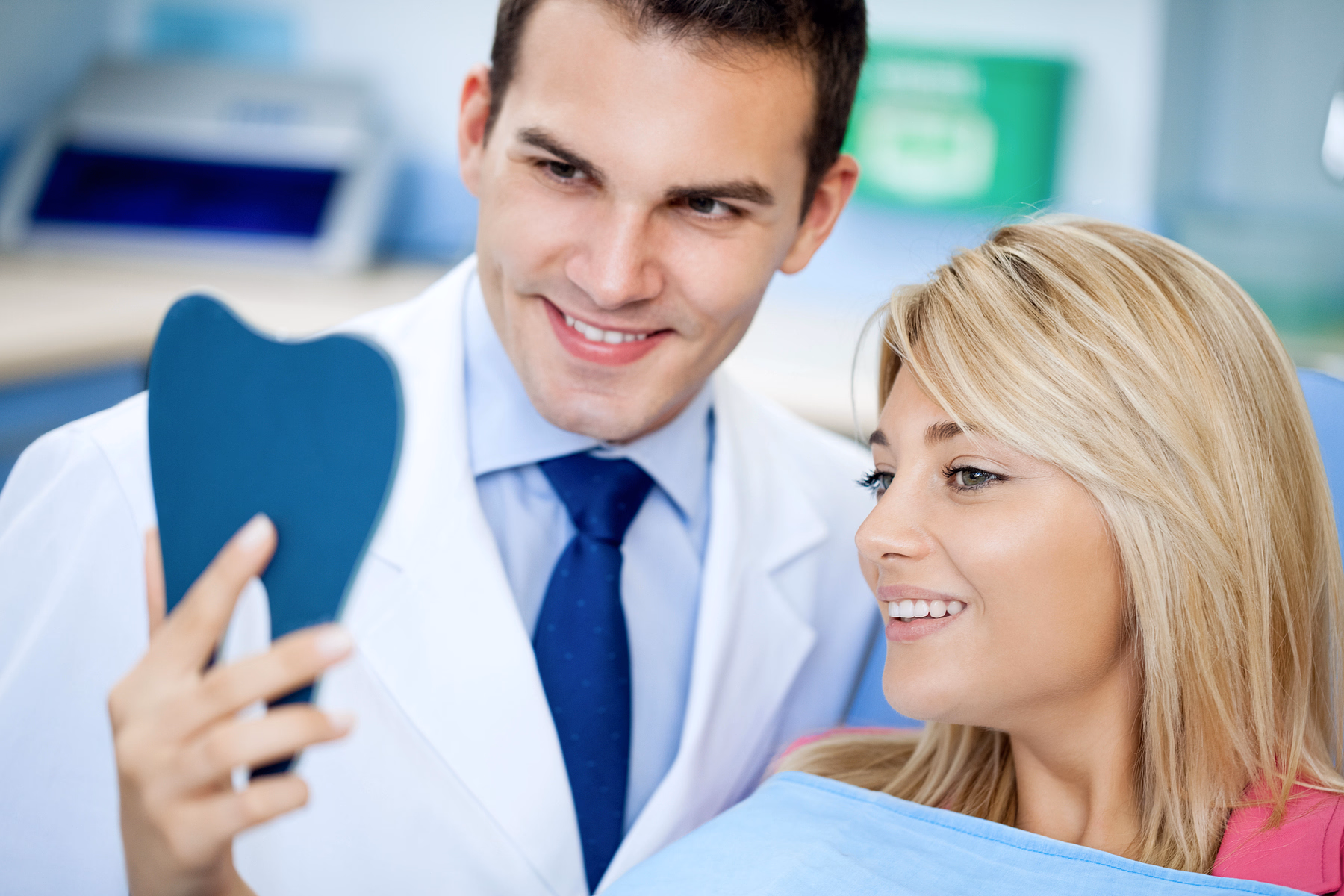 Dentist showing a smiling female patient a tooth-shaped mirror in a dental clinic.