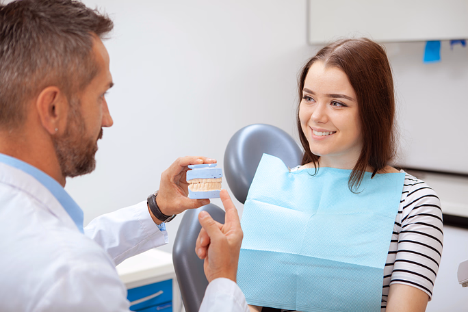 Dentista mostrando un molde dental a una paciente sonriente sentada en una silla dental.
