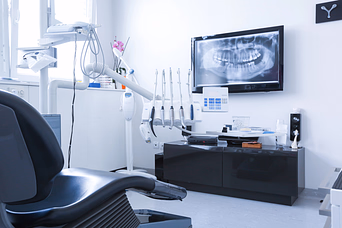 Modern dental clinic room with a dental chair, dental equipment, and a wall-mounted screen displaying a dental X-ray.