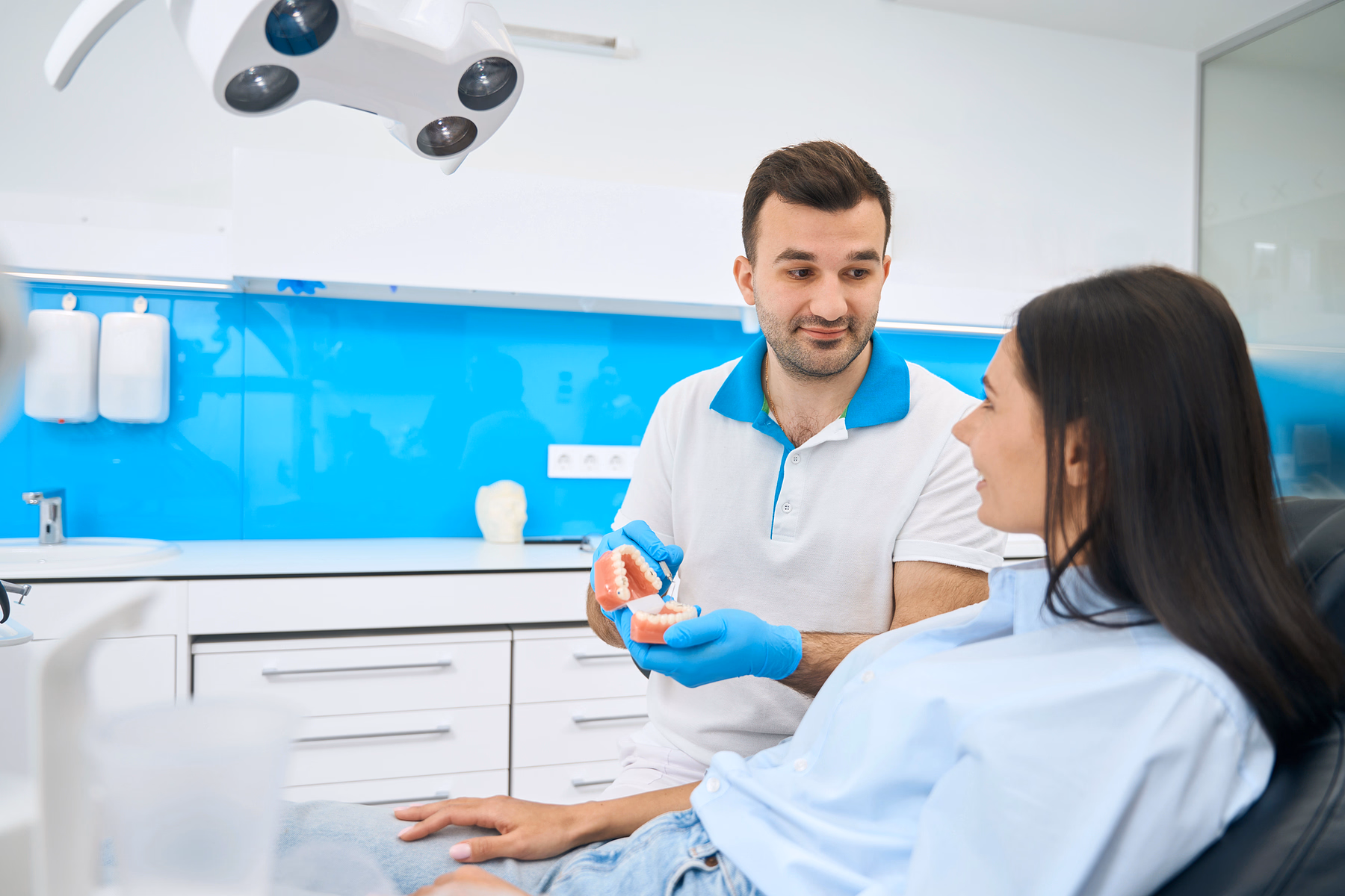 Dentist showing a dental model to a female patient in a brightly lit dental office.
