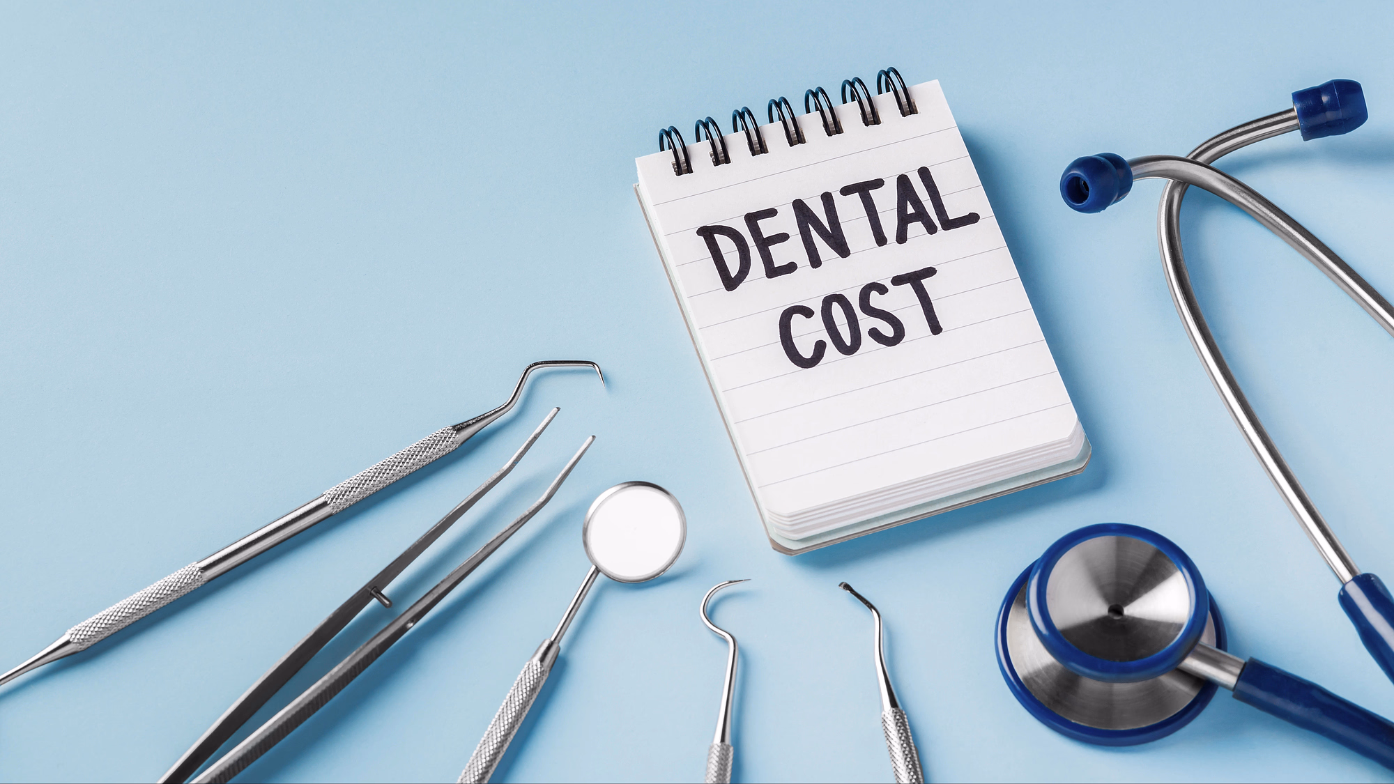 Dental tools and stethoscope surrounding a notepad with the words 'DENTAL COST' written on it against a blue background.