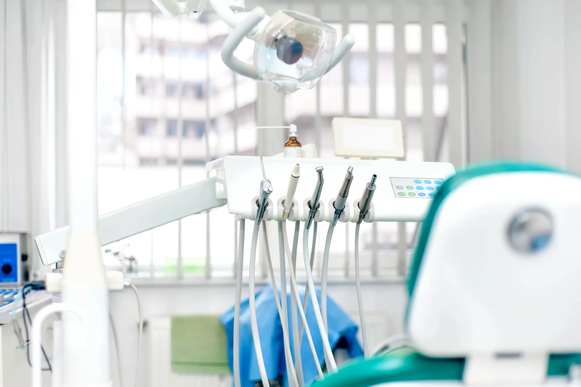 Close-up of dental instruments and tools attached to a dental chair in a bright clinic room.