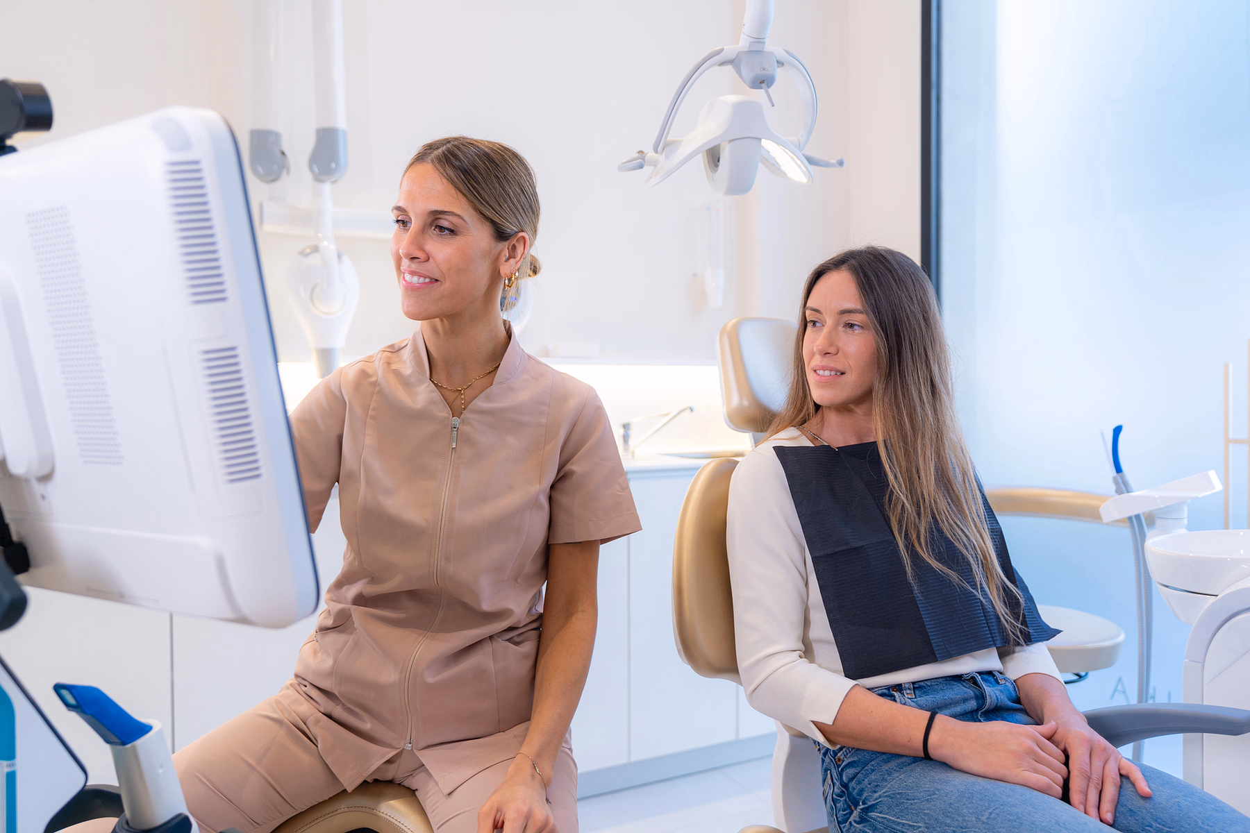 Dentist showing dental images on a monitor to a female patient seated in a dental chair.