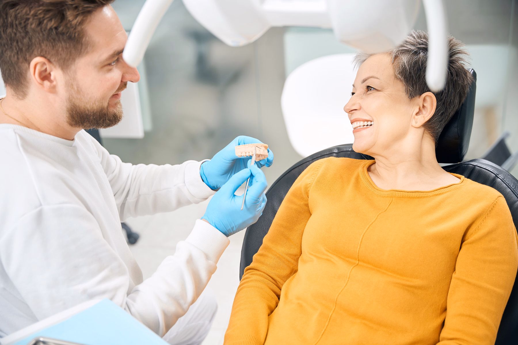 Dentist in blue gloves showing a dental mold to a smiling patient in a dental chair.