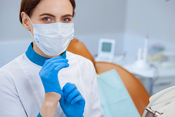 Healthcare professional wearing a face mask and blue gloves preparing for a procedure in a clinical setting.