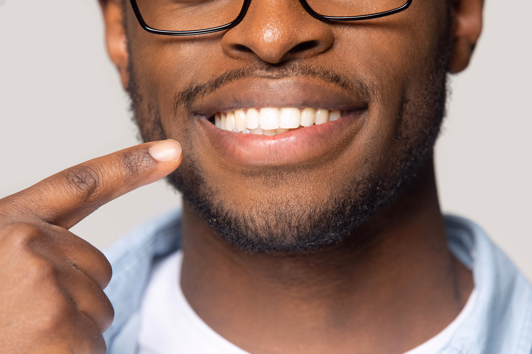 Close-up of a man with glasses smiling and pointing to his clean white teeth.