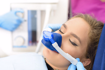 Medical professional placing an oxygen mask on a woman's face, who is lying down with eyes closed.
